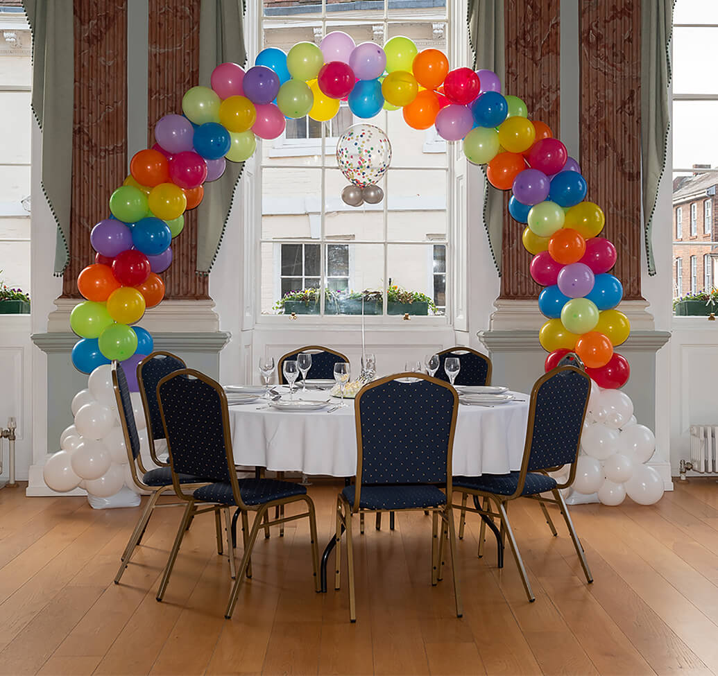 A rainbow balloon arch behind a decorated table